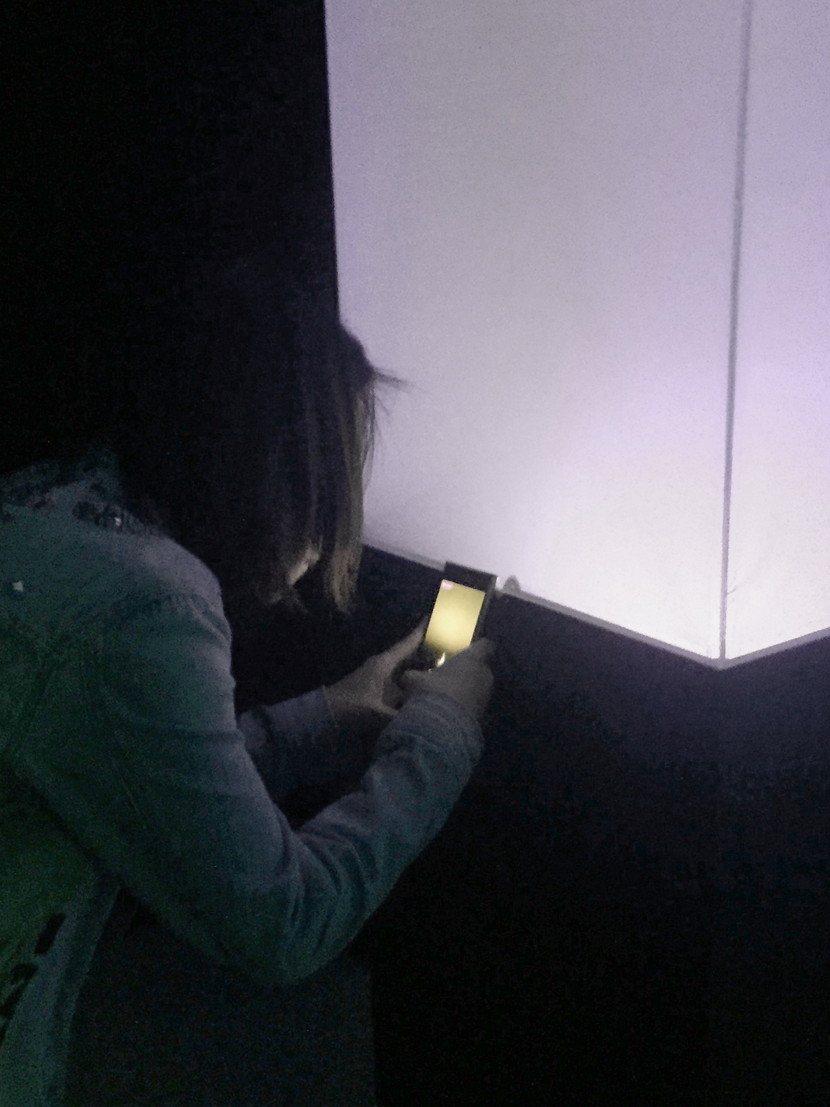 A girl holding a phone very closely to the glowing cube