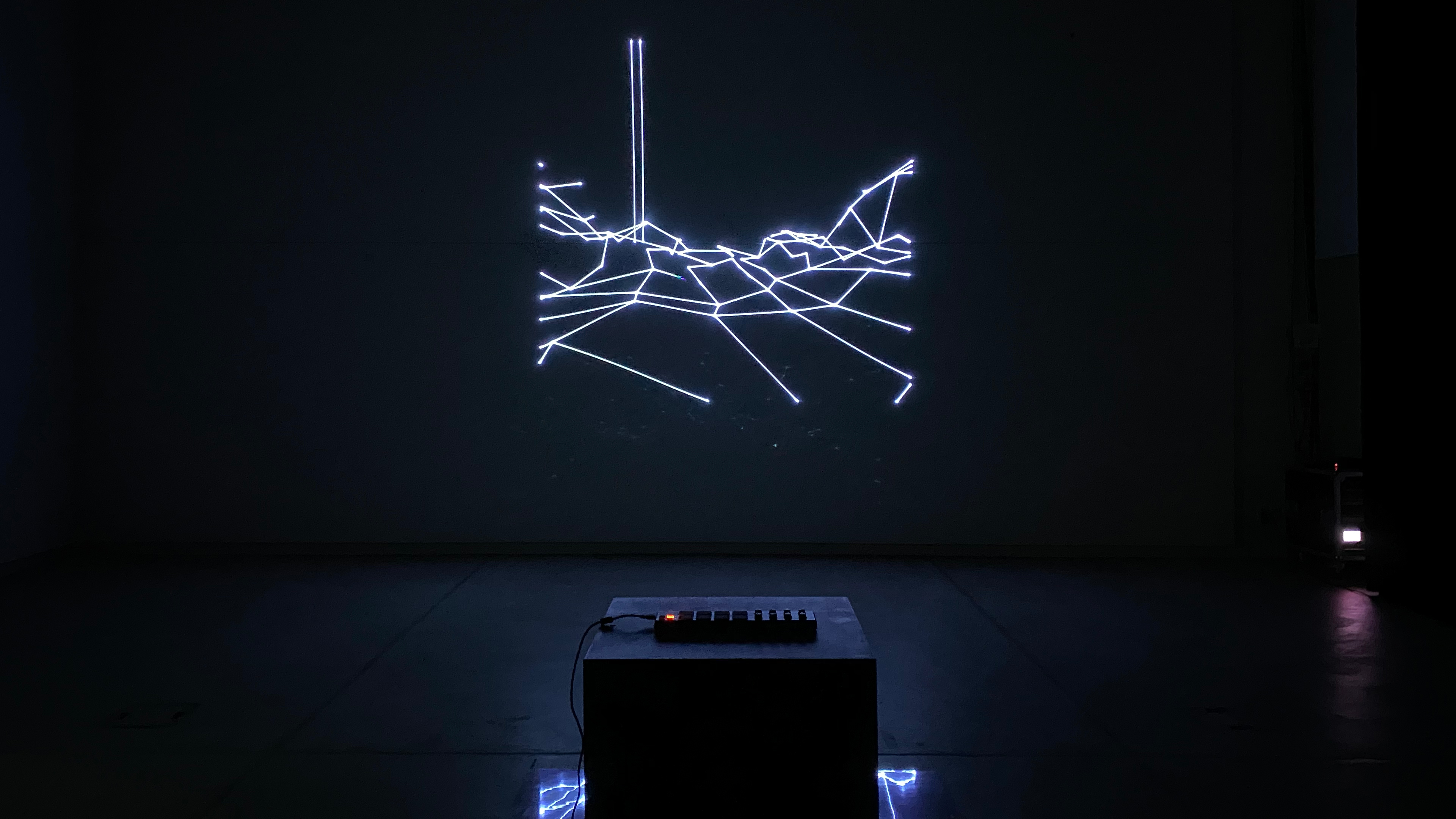 A laser projection onto a wall in a dark room. White lines showing an abstract landscape.