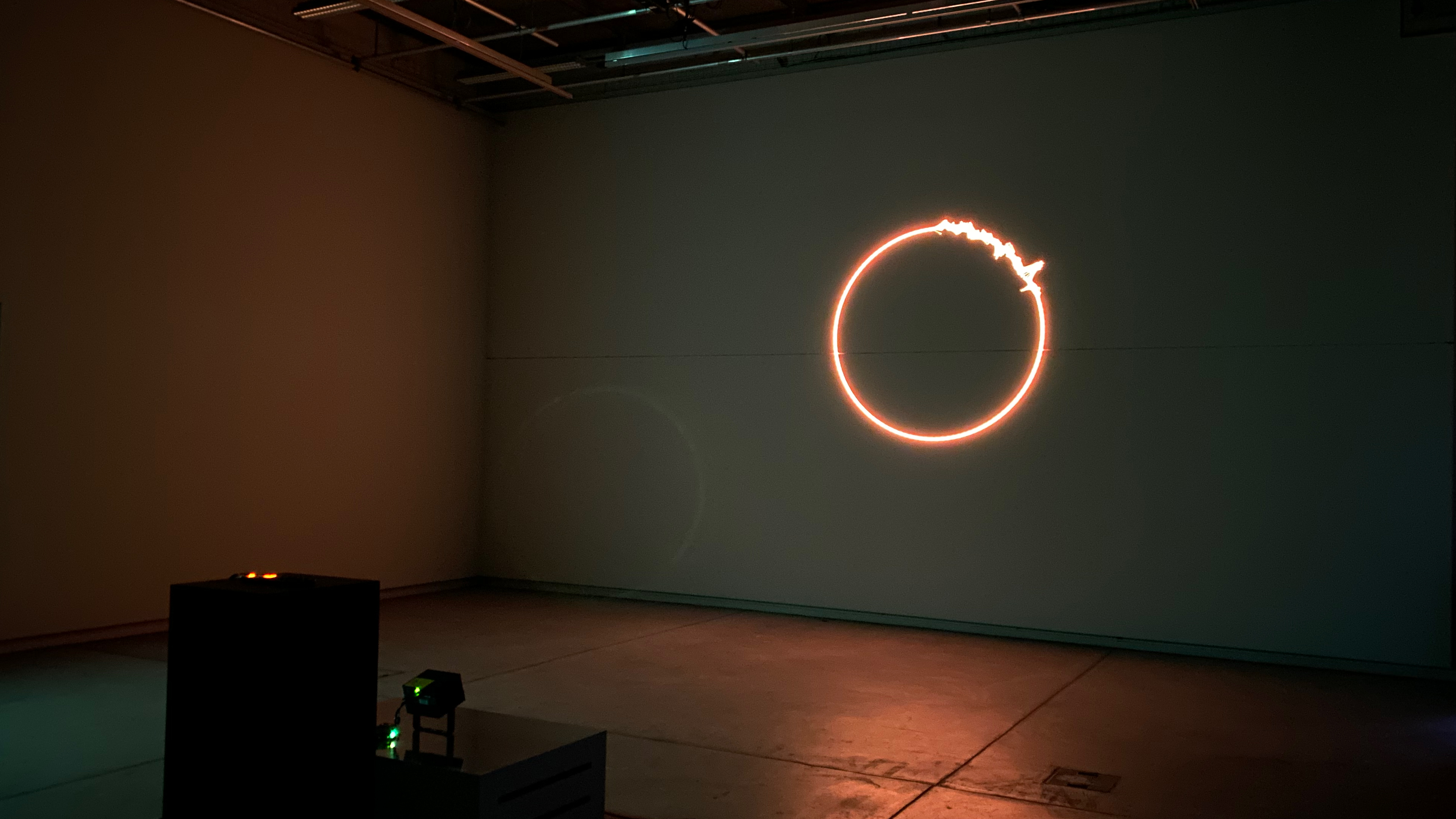 A laser projection onto a wall in a dark room. A red, disintegrating circle.